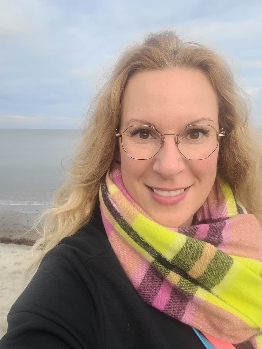 Alexandra Georg lächelt am Strand, mit Brille und buntem Schal